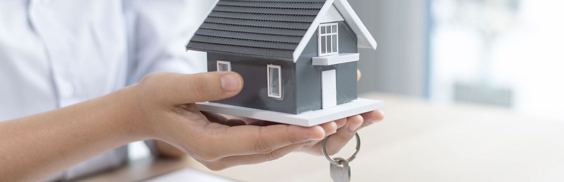 Asmuo laiko namelio muliažą, raktus ir dokumentus, simbolizuojančius būsto paskolos gavimą