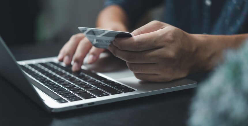 Mokėjimo kortelė rankoje ir nešiojamasis kompiuteris, atliekamas mokėjimas internetu